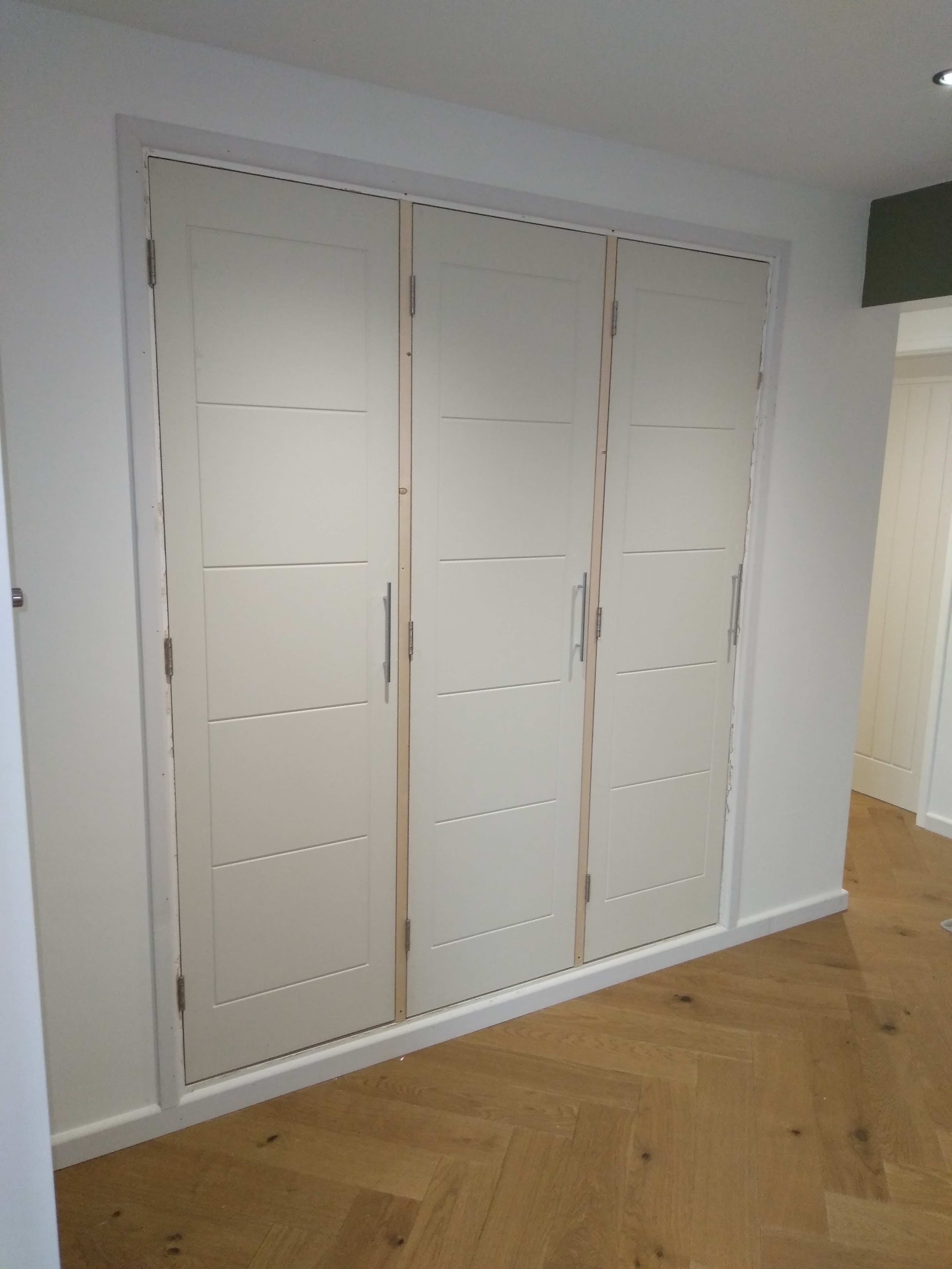 Three painted panel doors fitted as a built-in cupboard front above an oak herringbone floor