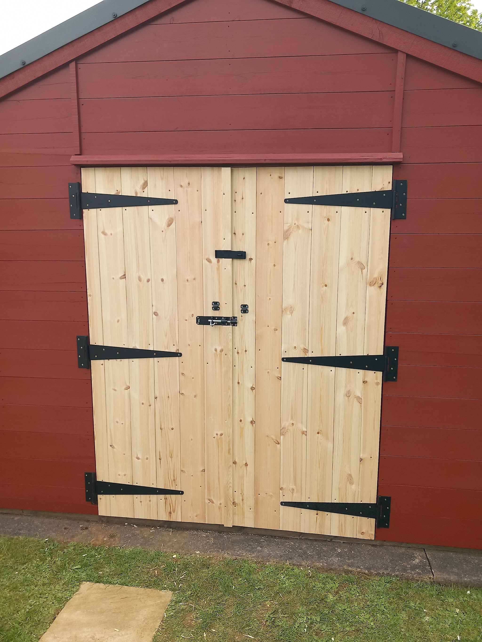 New ledged pine double doors with black T-hinges on a red-painted timber workshop