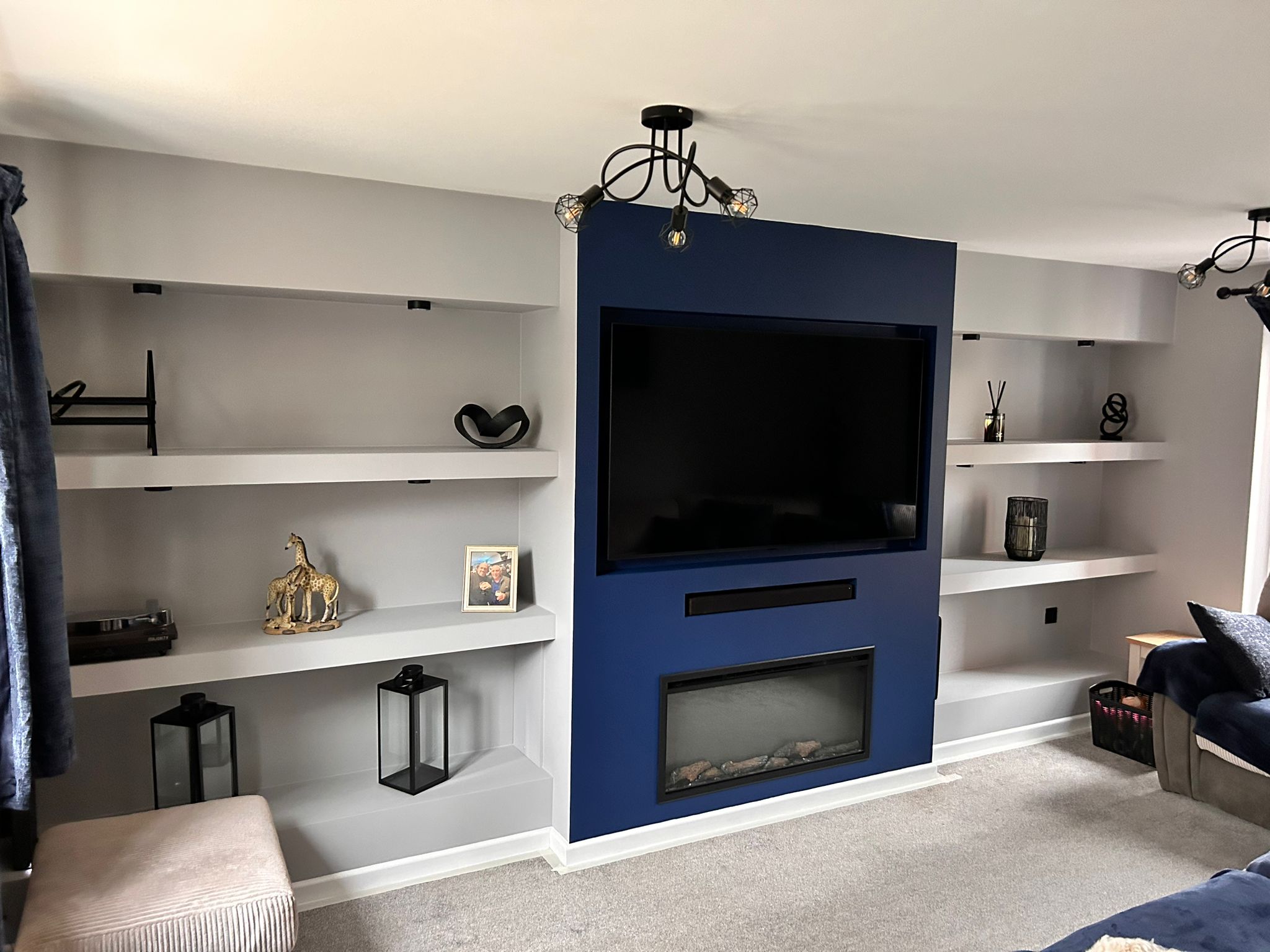 Living room media wall with a navy chimney breast, recessed TV and fire, and grey floating shelves in both alcoves