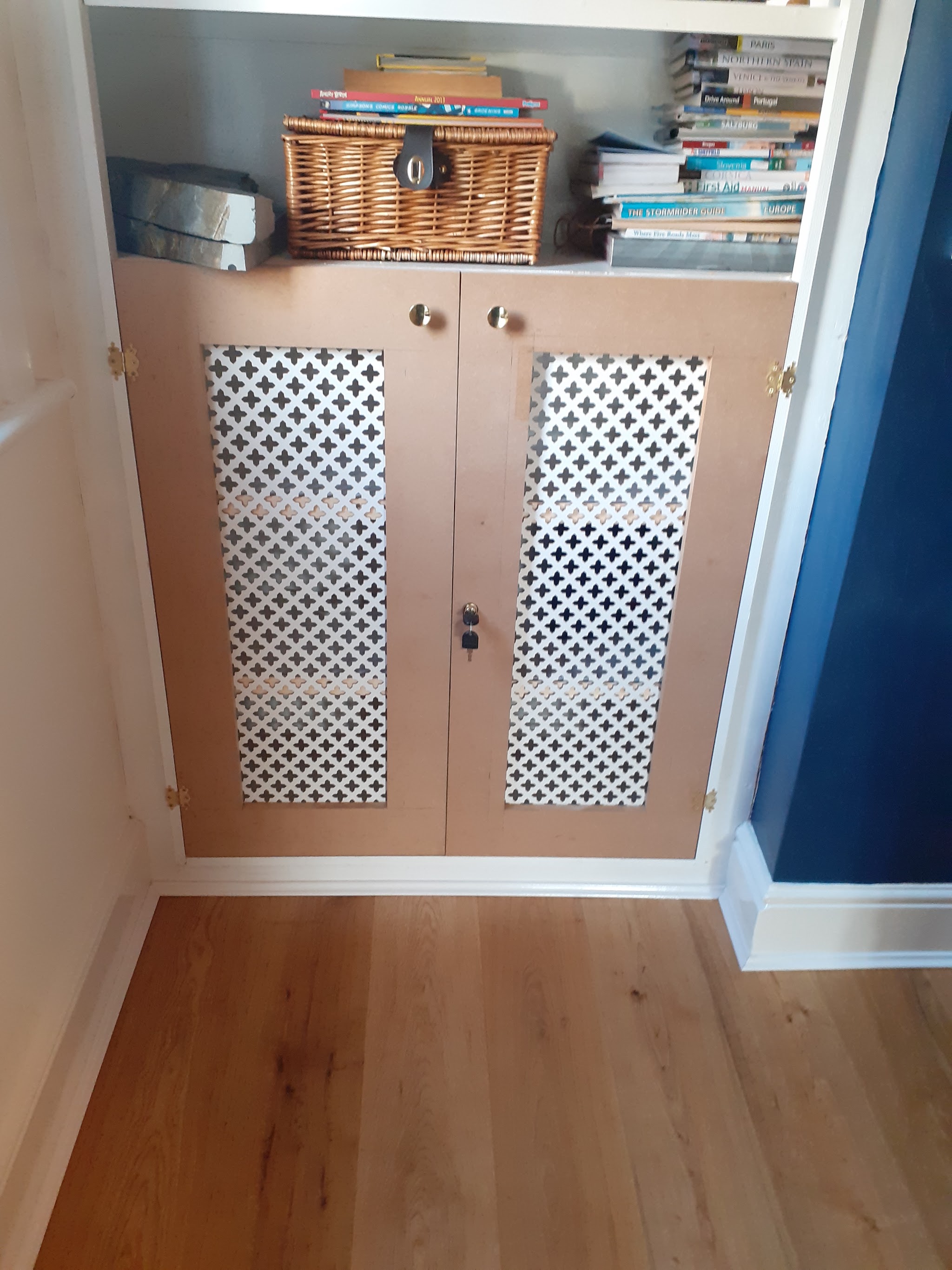 Alcove cupboard with doors and decorative metal grille panels beneath shelving