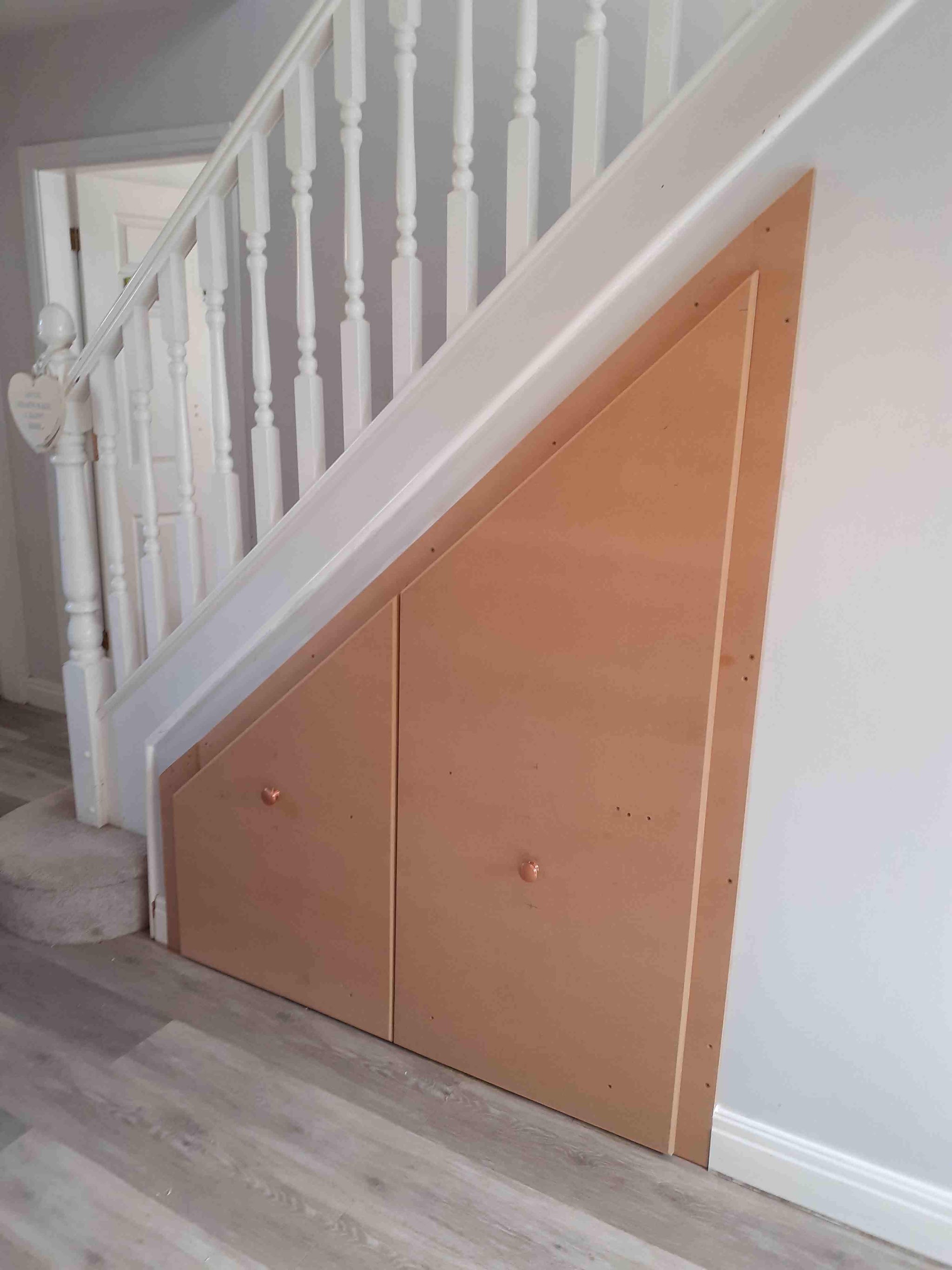 Angled storage doors built into the space beneath a white staircase, ready for painting